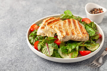 Fresh salad - cucumbers, tomato, arugula, chards leaves and chicken fillet grill in a plate on the table.  Healthy diet food.
