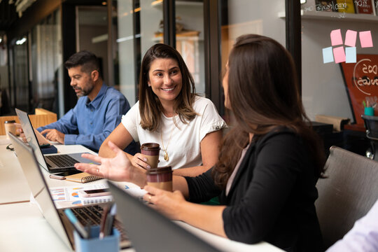 brazilian woman talking causally with co-worker in workstation. .