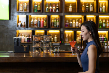 Young Asian woman with a sad face drinking cocktails in front of a vintage bar, Relaxing activities after work or hangouts, Place of entertainment for young adolescents or night club party.