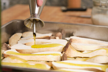 Close-up of olive oil being poured over sliced raw king trumpet mushrooms (pleurotus eryngii). Cooking process. Mediterranean diet.