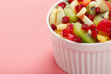 Salad of different juicy ripe fruits in a white cup on a pink background.