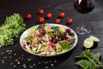 Salad with sliced meat, cheese, vegetables and salad mix on a white plate on a wooden table. Salad on a beautiful background with a glass of wine, lime, cherry tomatoes, pumpkin seeds and lettuce.