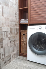Scandinavian Interiors of laundry room. Wicker laundry basket and clean cotton towels in a wooden closet near a Modern washing machine in a laundry room.
