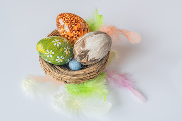 Easter eggs in a basket on a white background with a few colored feathers 