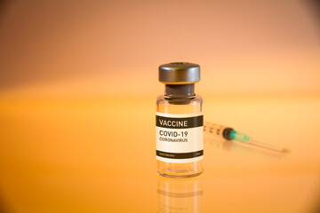 Covid-19 vaccine bottle and syringe on a yellow background