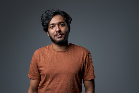 Portrait of a fashionable and bearded hindu dressed in modern clothing which poses in gray background looking at camera.