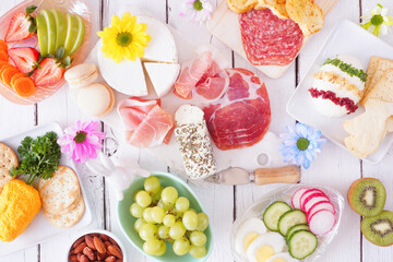 Spring or Easter theme charcuterie table scene against a white wood background. Assortment of cheese, meat, fruit and vegetable appetizers. Above view.