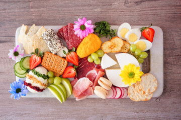 Spring or Easter theme charcuterie board against a wood background. Variety of cheese, meat, fruit...