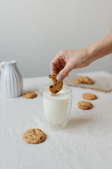 Female hand dipping cookies in milk. . Glass glass with milk and cookies.