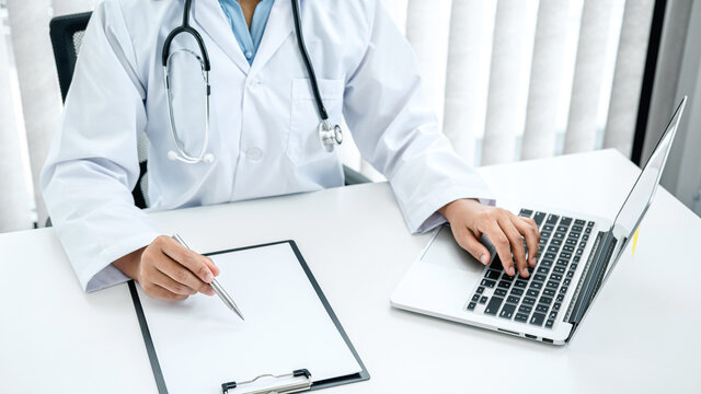 Doctor Hold Pen To Record Patient Data On Clipboard And Computer