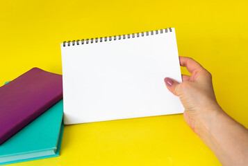 A female hand holds a large spiral notepad as a mockup for your design. Yellow background.