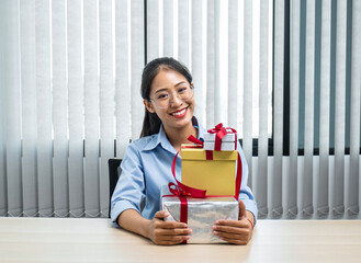 Young asian woman smiling and holding with many gift box at office workspace