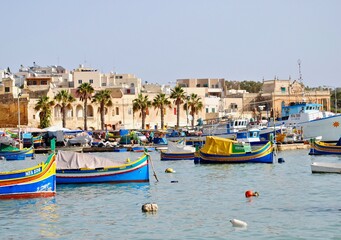 Fototapeta na wymiar Marsaxlokk, Malta: Maltese boats – the Luzzu and the Dgħajsa - float in the harbor of Marsaxlokk, Malta. the fishing boats are decorated with the eye of Osiris to keep the fishers safe at sea. 