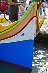 Fototapeta na wymiar Maltese boats – the Luzzu and the Dgħajsa - float in the harbor of Marsaxlokk, Malta. the fishing boats are decorated with the eye of Osiris to keep the fishers safe at sea. 