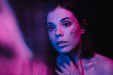Photo of a sensitive woman at a night party in a dark room in purple and blue light, has a bright...