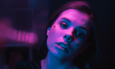 Cinematic portrait of an attractive woman in blue and purple light at a party, looking at the camera, she has a bright make-up with glitter.