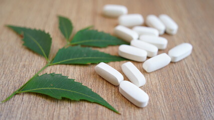 Fototapeta na wymiar Heap of calcium, vitamin supplement tablets with neem leaf isolated on wooden background. Many medical white pills and capsules for strong bones. Stay safe and healthy concept. coronavirus in India.