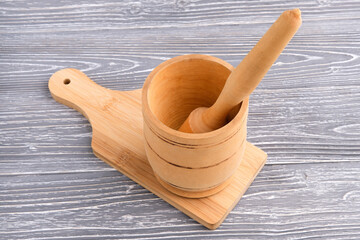 A wooden pusher lies in a round bowl that sits on a kitchen cutting board. Gray textured table....