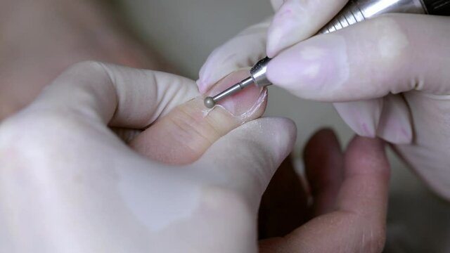 Processing of rough cuticles and lateral folds of fingernails with a round instrument. Medical hardware manicure in a beauty salon.