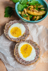 Traditional Scottish meat cutlet with boiled eggs, cucumber and parsley on cutting board.