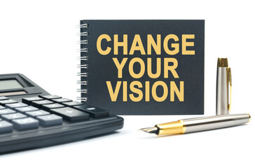 On a white background, there is a calculator, a pen and a black notebook with the inscription - CHANGE YOUR VISION