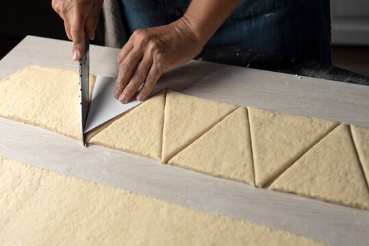 hands cutting the croissant dough with a knife and croissant into triangles to assemble and bake