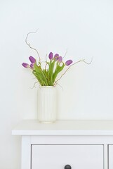 bouquet of tulips in a white vase on a white chest of drawers
