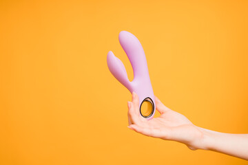 Sex gadgets and masturbation devices. Pink dildo in woman's hand on orange background. sex toys:...
