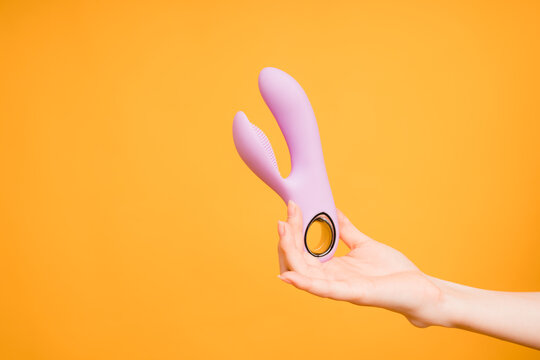Sex gadgets and masturbation devices. Pink dildo in woman's hand on orange background. sex toys: anal butt plugs, vibrators, vaginal balls. Top view