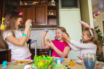 three girls with painted Easter eggs in their hands are laughing and fooling around at home in the kitchen