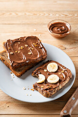Fresh toasts with chocolate spread and slices of banana on a gray plate on a wooden background