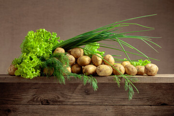 Young fresh organic potatoes with dill, salad and onion on a old wooden table.