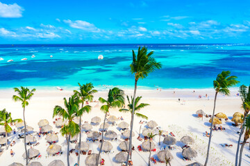 Beach vacation and travel background. Aerial drone view of beautiful atlantic tropical beach with straw umbrellas, palms and boats. Bavaro beach, Punta Cana, Dominican Republic. - obrazy, fototapety, plakaty