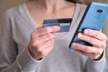 Online shopping concept. Female holding credit card while using her smart phone for inputting card information and making payment. Lifestyle and technology. Close up.