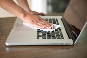 Close up of woman’s hands disinfecting her laptop with personal sanitizer spray.