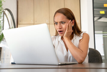 Woman in front of the laptop looking terrified and worried.