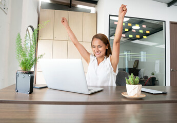 Successful woman raising hands in front of her computer celebrating good results
