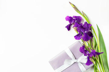 A bouquet of iris flowers and a wrapped gift with a silver ribbon are on a white background. Holiday greetings theme. Free space for text.