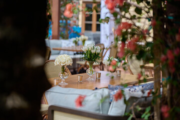 Table setting with candles and vases with white flowers, bushes with flowers on the foreground