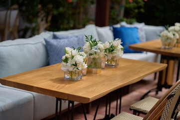 Vases with bouquets of white flowers on the table with blue couch on the background