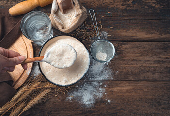 The cook's hand stirs the leaven. Flour, sourdough, water, wheat on a wooden background. Cooking...