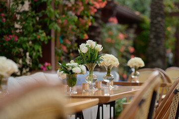 Vases with bouquets of white flowers on the table, bushes with flowers in the background