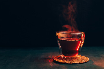 Hot freshly brewed black tea in a glass cup on a dark background, a mug of tea with steam coming out of it.