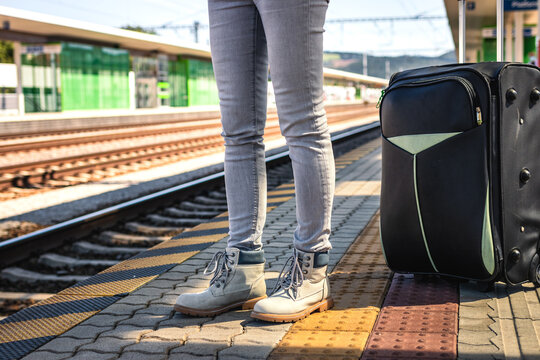 Woman with suitcase waiting at railroad station platform. Travel to vacation with large luggage by train