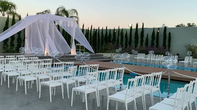 Jewish traditions wedding outdoor ceremony. Wedding canopy (chuppah, hupa) made of white fabric against the background of evening sky, palms and an artificial reservoir decorated with balloons. HD