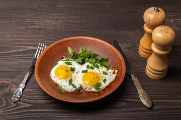 fried eggs with herbs on a clay plate on a dark wooden table