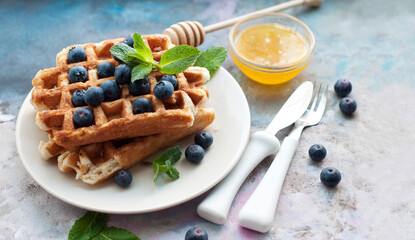 Belgian waffles with blueberries, honey and mint on a white plate. Knife and fork with white handles