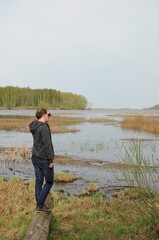 A young man stands on the shore of a reservoir and looks into the distance. Comfortable sportswear for every day. Overgrown lake. 