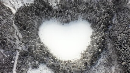 Heart shaped lake in winter forest. Tilting drone shot of natural snow wonder nature environment. Love peace save our planet symbol sign in Swedish woods. frozen pond water special shape Sweden 