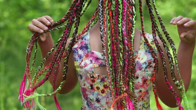 A teenage girl is touching her multi-colored dreadlocks.